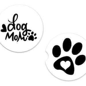 May include: Two white round coasters with black designs. One coaster features the text "Dog Mom" with a small paw print. The other coaster features a black paw print with a white heart in the center.
