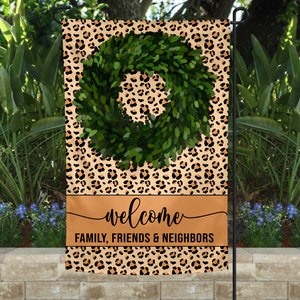 May include: A welcome garden flag with a leopard print background and a green wreath. The flag has the text "Welcome Family, Friends & Neighbors" printed on it.