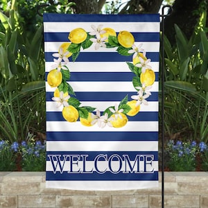 May include: A white and blue striped garden flag with a wreath of lemons and white flowers. The flag says "WELCOME" in blue letters.