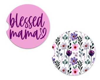 May include: Two round pink and white coasters. One coaster has the text "blessed mama" in purple lettering with a heart. The other coaster has a floral pattern with purple, pink, and green flowers.