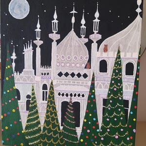 Könnte beinhalten: Acrylbild zeigt einen weißen Palast mit mehreren Türmen und Kuppeln vor einem schwarzen Nachthimmel. Grüne Weihnachtsbäume mit bunten Lichtern befinden sich im Vordergrund. Ein Vollmond und Sterne sind ebenfalls zu sehen.