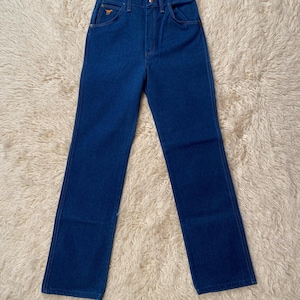 May include: A pair of blue denim jeans with a high waist and straight leg. The jeans have a classic five-pocket design, a button and zipper closure, and a small embroidered logo on the front pocket. The jeans are made of a sturdy denim fabric.