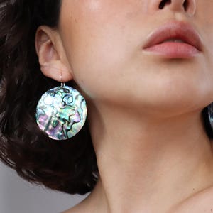 May include: Circular iridescent earrings with a swirling pattern of blues, greens, and purples. The earrings hang from silver-coloured hooks. These earrings are a statement piece, adding colour and texture.