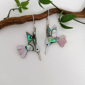 Peut inclure: Une paire de boucles d'oreilles en argent en forme de colibri avec des ailes en nacre d'ormeau irisées et des accents roses.