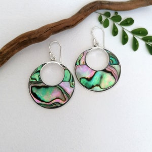 May include: A pair of silver hoop earrings featuring a green, pink, and iridescent abalone shell inlay. The earrings have a simple, elegant design.