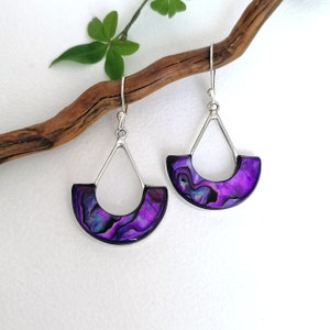 May include: A pair of silver dangle earrings featuring a purple abalone shell design. The earrings are teardrop shaped with a curved top and a straight bottom.