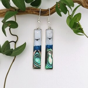 May include: Silver dangle earrings featuring a white, blue and green abalone shell design. The earrings are rectangular in shape and have a silver hook.