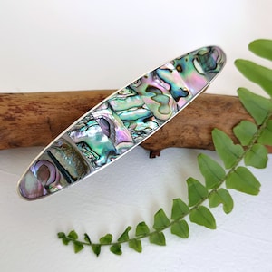 May include: A silver hair clip with a long oval shape and a design of iridescent abalone shell pieces.