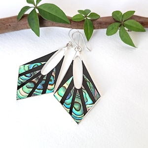 May include: A pair of diamond-shaped dangle earrings featuring iridescent abalone shell inlays set within black frames. The earrings have silver-toned metal borders and silver ear wires, with a central oval cutout at the top of each piece.