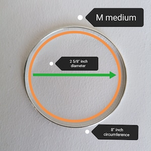 May include: A silver bangle bracelet with an orange inner circle. The bracelet is labeled "M medium" and has a diameter of 2 5/8 inches and a circumference of 8 inches.