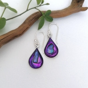 Könnte beinhalten: Ein Paar silberne Ohrhänger mit schimmernden, tropfenförmigen Anhängern aus irisierendem, violettem Abalone-Perlmutt.