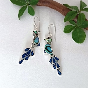 Op de afbeelding: Zilveren vogel oorbellen met abalone schelp en blauwe emaille accenten. De oorbellen, met een haaksluiting, tonen een gedetailleerd vogelontwerp. Een stijlvol accessoire dat een vleugje natuur toevoegt.