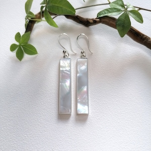 Puede incluir: Un par de pendientes de plata con piedras rectangulares de madreperla blanca.