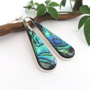 May include: A pair of silver teardrop earrings with iridescent abalone shell inlays. The earrings have a long, slender design and feature a natural, organic pattern.