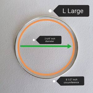 May include: A silver bangle bracelet with an orange inner circle. The bracelet is labeled "L Large" and has a diameter of 2 6/8 inches and a circumference of 8 1/2 inches.