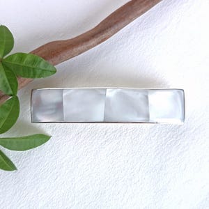 May include: A rectangular hair barrette featuring a silver-toned metal frame inlaid with four distinct, smooth, iridescent white mother-of-pearl panels arranged in a horizontal row, creating a reflective and polished surface appearance.