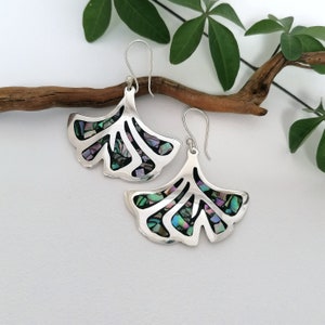 Peut inclure: Boucles d'oreilles en argent avec un motif de feuille de ginkgo. Les feuilles sont remplies de morceaux d'abalone iridescent.