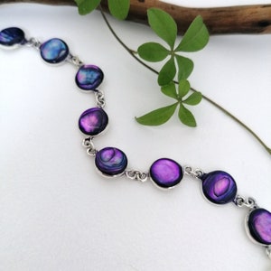 May include: A silver chain bracelet with round, iridescent purple and blue abalone shell charms.
