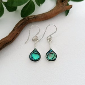 Könnte beinhalten: Ein Paar silberne Ohrhänger mit tropfenförmigen Anhängern aus Abalone-Muschel. Die Muschel hat eine grüne, blaue und irisierende Farbe.