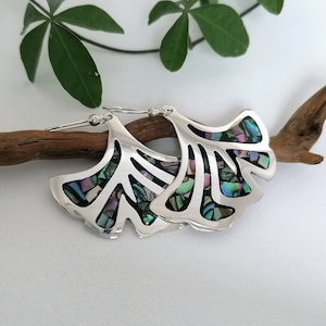 May include: A pair of silver earrings shaped like ginkgo leaves with iridescent abalone shell inlay.