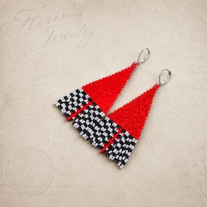 May include: A pair of handmade earrings with a geometric design. The top portion is red, transitioning to a black and white checkered pattern. The earrings are triangular and feature silver-colored ear wires. The text "Herinia Jewelry" is visible.