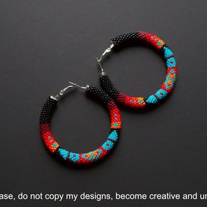 May include: A pair of large hoop earrings with a black, red, orange and turquoise beaded design.