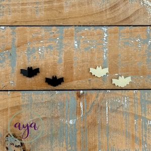 May include: Three bat-shaped cutouts on a wood background. Two are black and one is beige.