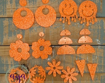 May include: Assortment of orange glitter acrylic earring blanks in various shapes, including circles, flowers, smiley faces, and triangles.
