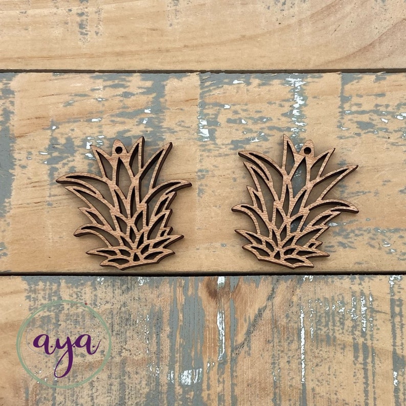 May include: Two wooden pineapple shaped ornaments with a cutout design. The ornaments are light brown in color and have a hole at the top for hanging.