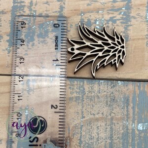 May include: A wooden cutout of a stylized pineapple with a hole at the top for hanging. The cutout is approximately 2 inches tall and is shown next to a ruler.