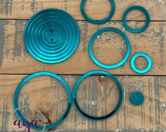May include: A set of teal metallic circle frames of various sizes. The frames are arranged on a wooden surface.