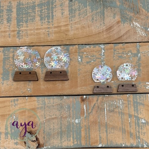 May include: Four iridescent clear plastic snow globes with snowflake designs on a wooden background. The snow globes are different sizes and are attached to wooden bases.