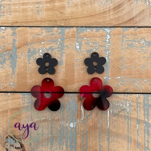 May include: Two pairs of flower-shaped earrings. One pair is black and the other pair is red with black accents.