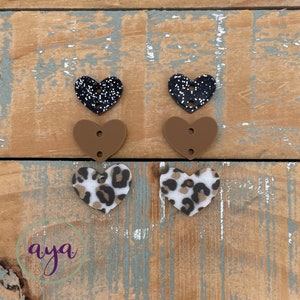 May include: Six heart-shaped resin embellishments in three different designs. Two black hearts with white glitter, two brown hearts, and two brown and white leopard print hearts.