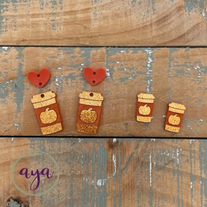 May include: A set of five fall-themed acrylic charms. Two red heart charms, two orange coffee cup charms with a pumpkin design, and one smaller orange pumpkin charm.