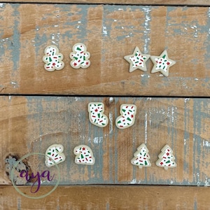 May include: Assortment of Christmas cookie-shaped ornaments with red and green sprinkles. The ornaments are in the shapes of gingerbread people, stars, stockings, and Christmas trees.