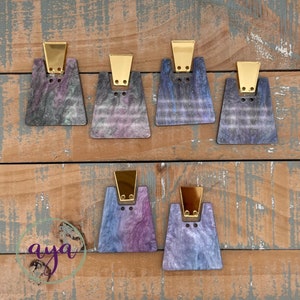 May include: Five pairs of geometric shaped earrings with a marbled effect in shades of purple, blue, and black. The earrings have a gold-colored metal top.
