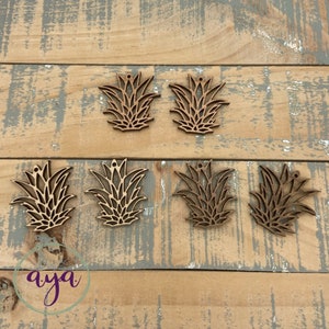 May include: Six wooden pineapple-shaped ornaments with a hole at the top for hanging. The ornaments are a light brown color and have a detailed design.