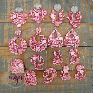May include: A collection of red and white Halloween-themed earrings and charms. The designs include skulls, skeletons, and various shapes like bats, cats, and teardrops. The earrings have silver-colored hardware.