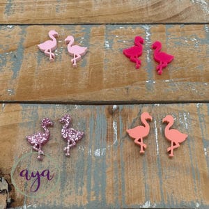 May include: A set of six pink flamingo earrings. Two pairs are solid pink, one pair is a light pink, and one pair is a glittery pink.