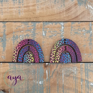 May include: Two rainbow-coloured wooden arches with a leopard print pattern. The arches are layered on top of each other, creating a three-dimensional effect.