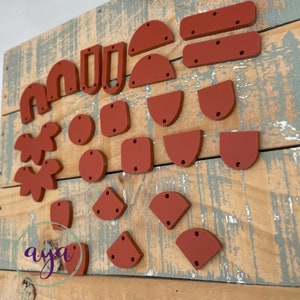 May include: A collection of 25 terracotta-colored wooden shapes, including circles, squares, rectangles, semicircles, and irregular shapes. Each shape has two or three small holes drilled through it.