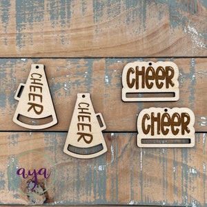 May include: Two wooden megaphone ornaments with the word "CHEER" engraved on them. Two wooden rectangular ornaments with the word "CHEER" engraved on them.