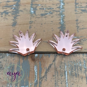May include: Two rose gold acrylic shapes with a starburst design. Each shape has two holes for attaching to a project.