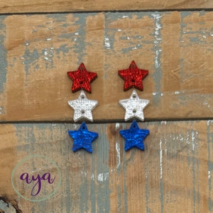May include: Six glittery star-shaped embellishments in red, white, and blue. The stars are arranged in three rows of two.