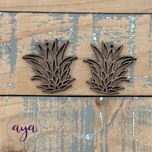 May include: Two brown wooden pineapple-shaped ornaments with a hole at the top for hanging.