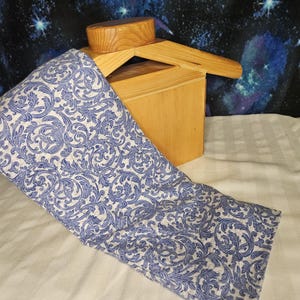 May include: A blue and white patterned fabric wrap is draped over a wooden box. The fabric features a detailed, swirling design. A small, round wooden piece sits atop the box. The background is a starry night sky.