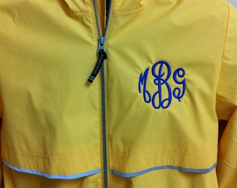 May include: A bright yellow hooded windbreaker jacket featuring a full-length grey front zipper with a black pull tab labeled Charles River. The jacket displays a blue embroidered monogram on the left chest and a horizontal grey reflective stripe.