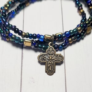 May include: A multi-strand bracelet with blue, green, and gold beads. The bracelet has a small, gold cross charm.