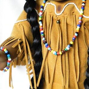 May include: A doll wearing a brown suede fringed outfit with a colorful beaded necklace and bracelet.